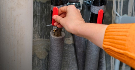 Woman turning red valve on pipe, controlling water supply.